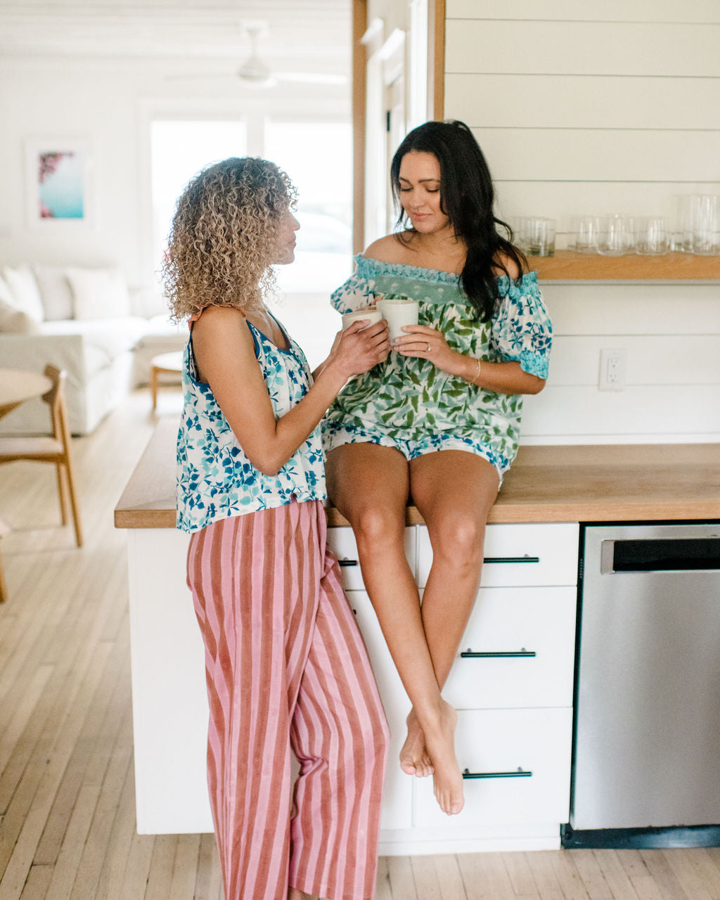Two Woman having coffee in the kitchen wearing the Sundara pajama sets – soft cotton sleepwear with hand-block prints, blending comfort and casual elegance.