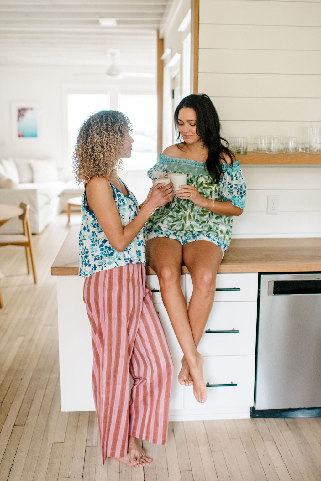 Two Woman having coffee in the kitchen wearing the Sundara pajama sets – soft cotton sleepwear with hand-block prints, blending comfort and casual elegance.