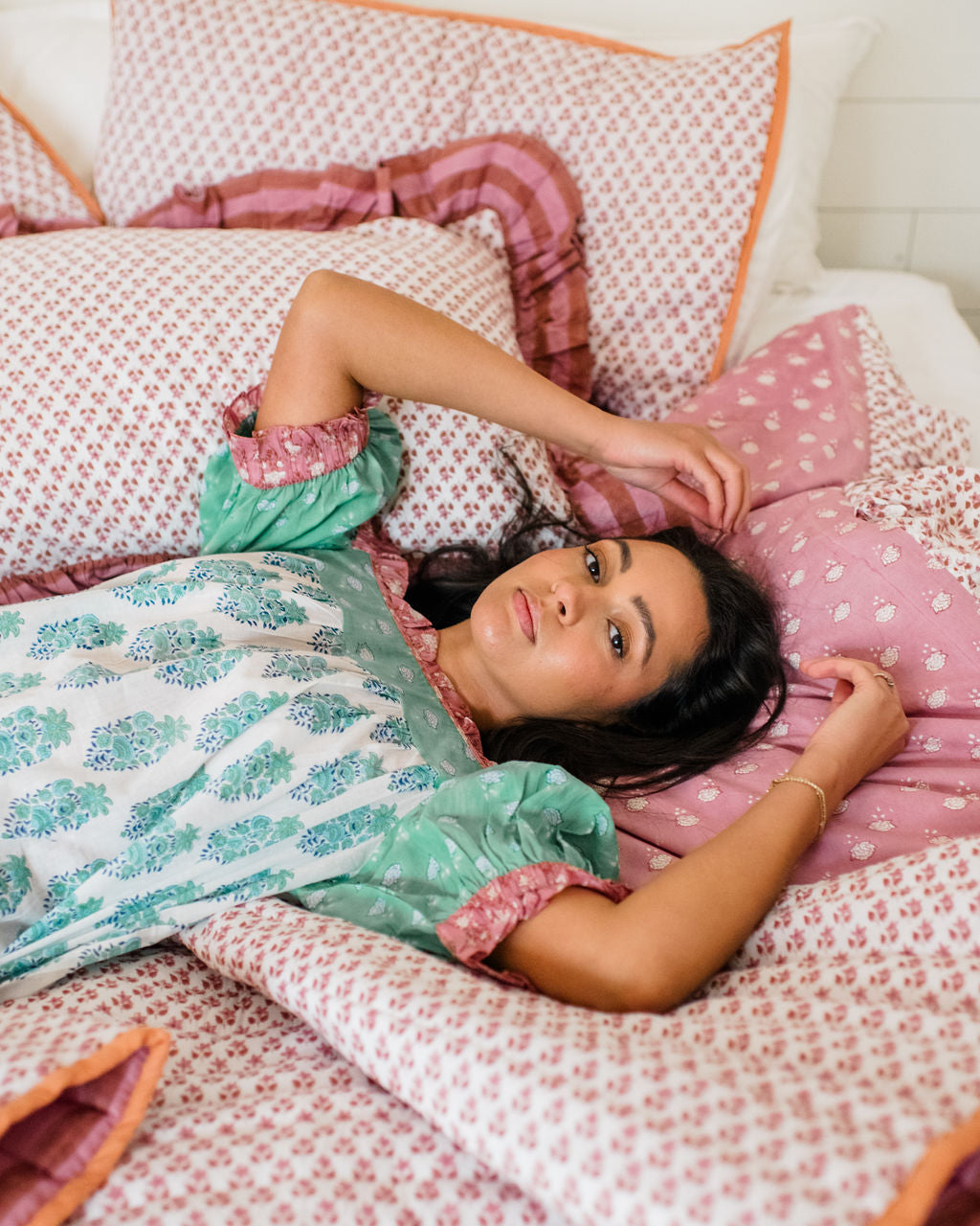 The Winnie Top by Sundara – a relaxed cotton pajama top with block prints, styled with a woman lounging on Sundara’s luxurious bedding, including quilts and shams for ultimate comfort and style.