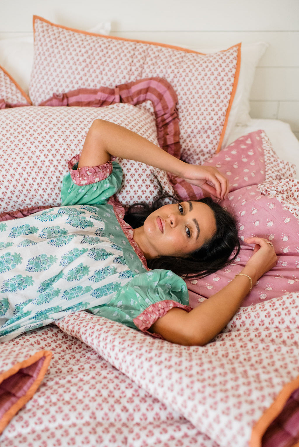 The Winnie Top by Sundara – a relaxed cotton pajama top with block prints, styled with a woman lounging on Sundara’s luxurious bedding, including quilts and shams for ultimate comfort and style.