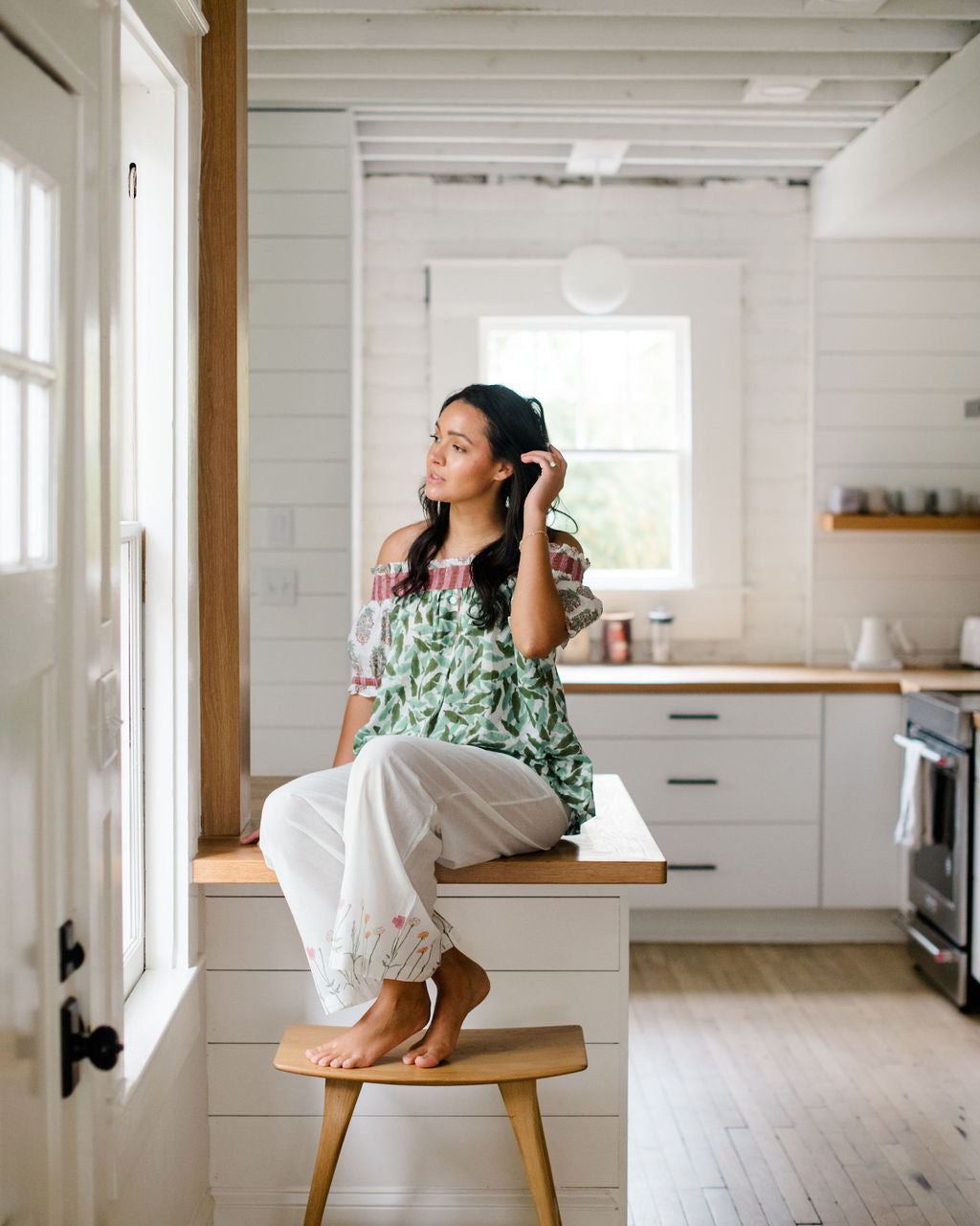 Woman sitting on a kitchen counter in the Winniepajama top and Logan pant by Sundara – soft cotton sleepwear with hand-block prints, blending comfort and casual elegance.