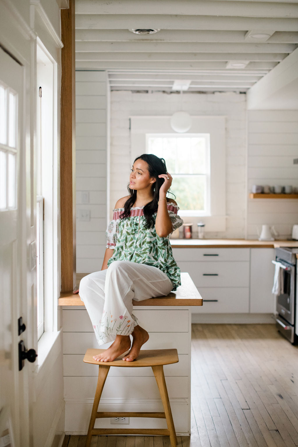 Woman sitting on a kitchen counter in the Winniepajama top and Logan pant by Sundara – soft cotton sleepwear with hand-block prints, blending comfort and casual elegance.