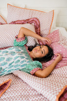 The Winnie Top by Sundara – a relaxed cotton pajama top with block prints, styled with a woman lounging on Sundara’s luxurious bedding, including quilts and shams for ultimate comfort and style.